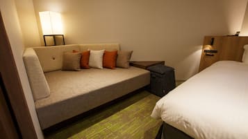 A hotel room with a sofa, a bed, a nightstand, and a lamp.