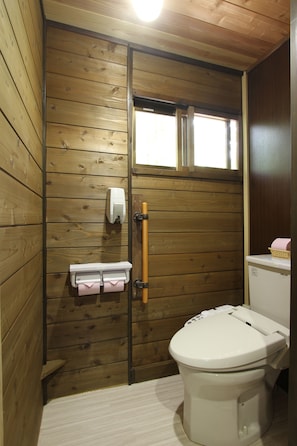 A wooden-paneled bathroom with a toilet, a hand dryer, and a paper towel dispenser.