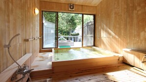 A wooden spa room with a large hot tub, a shower area, and a view of a backyard through a sliding glass door.