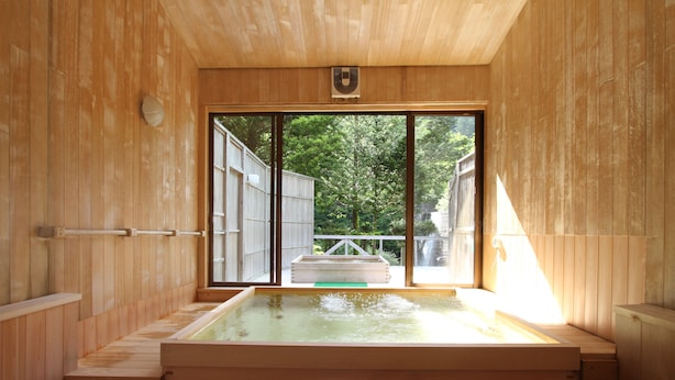 A wooden spa room with a hot tub, large sliding glass doors, and a view of a wooden deck and trees outside.