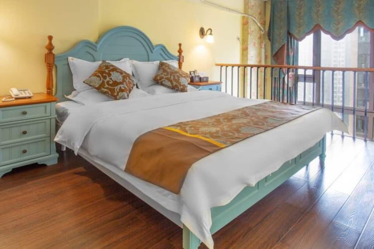 A bedroom with a bed, nightstands, a wooden headboard, a window with curtains, and a balcony railing.