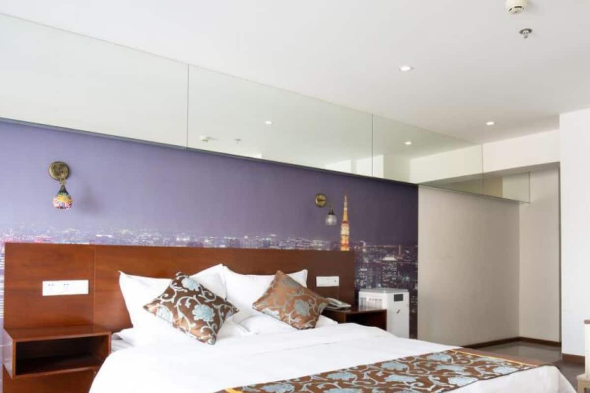 A modern hotel room with a large bed, wooden headboard, and a cityscape mural on the wall.