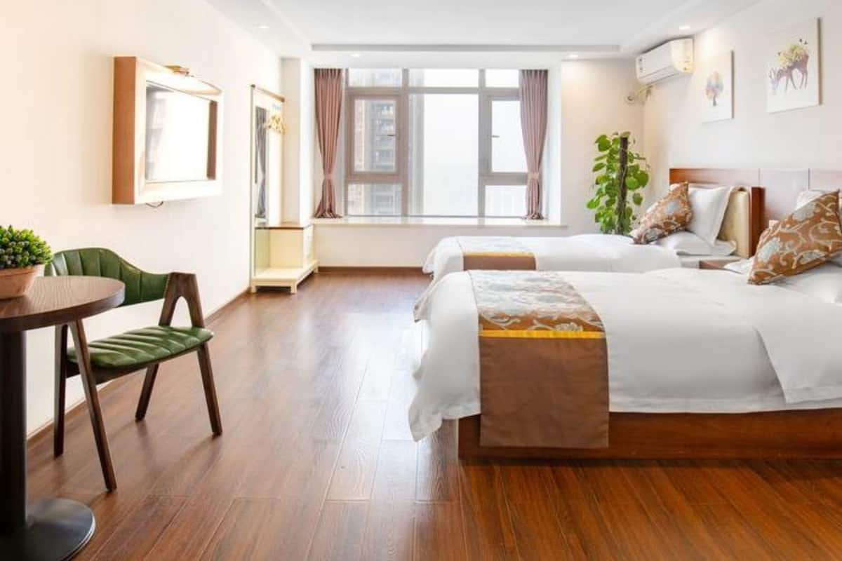 A hotel room with two beds, a dining table, a chair, and a window with curtains.