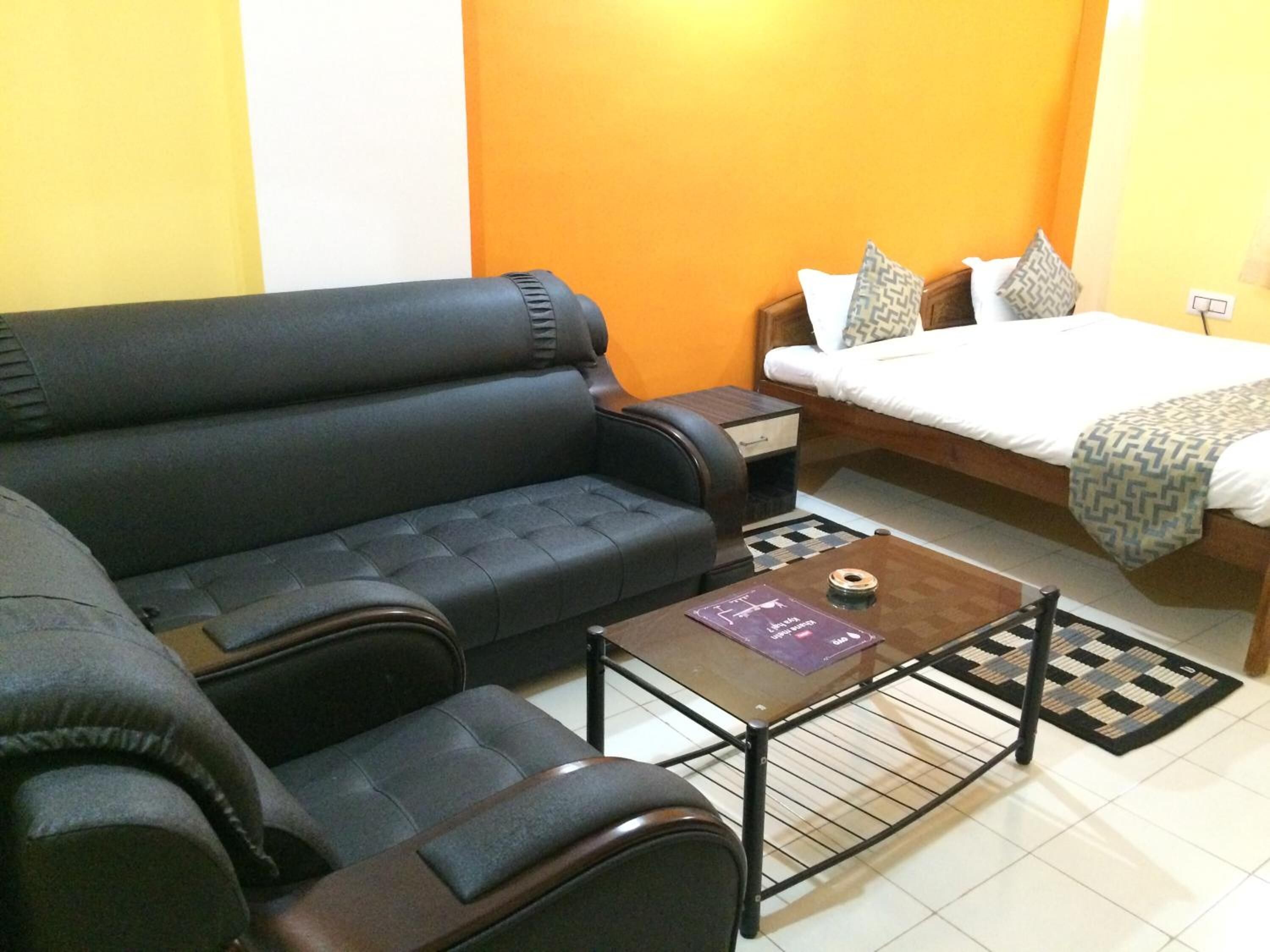 A compact room with a sofa, a small table, a bed with patterned bedding, and a nightstand.