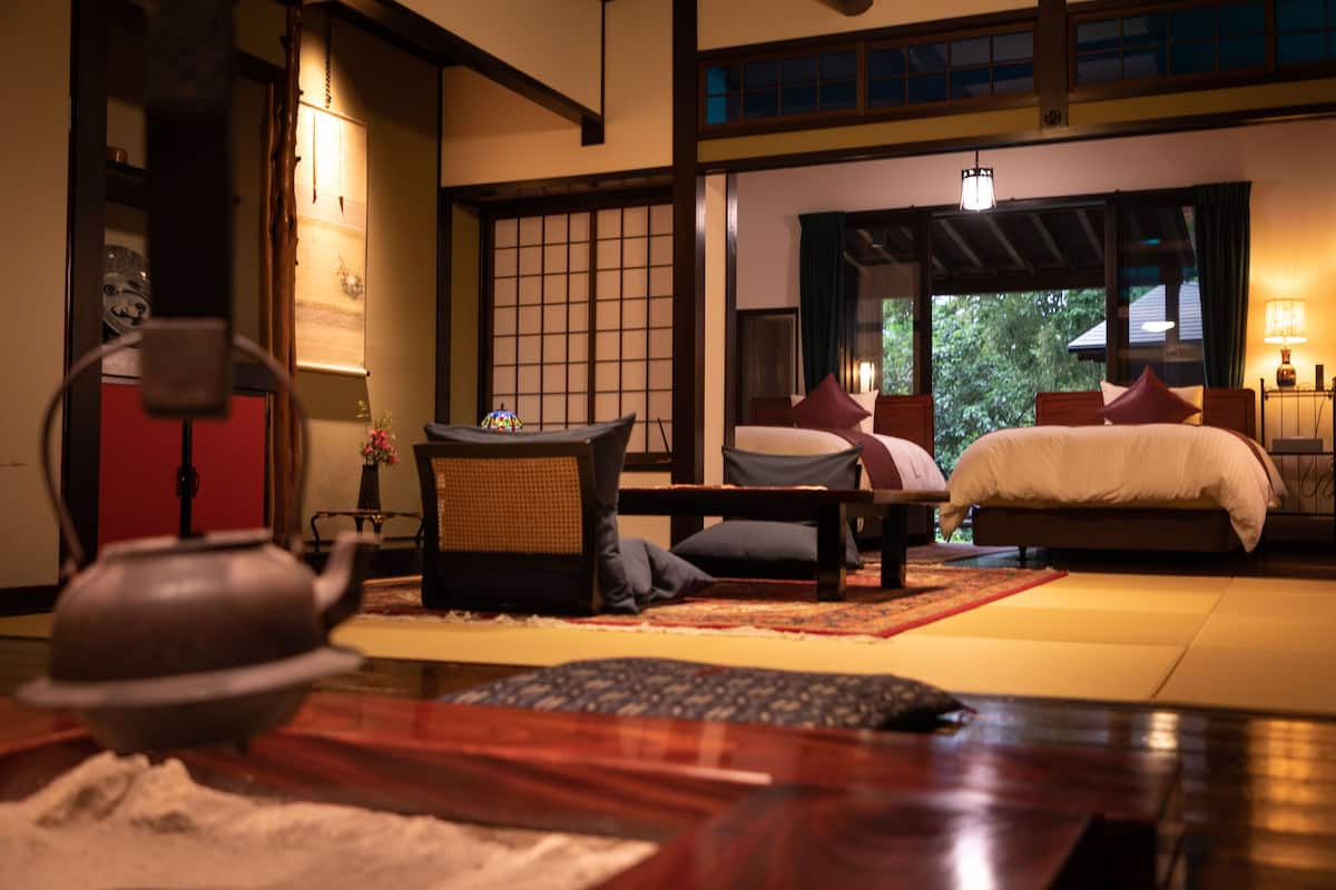 A traditional Japanese-style room with tatami flooring, a low wooden bed with pillows, a tea set, and a shoji screen.