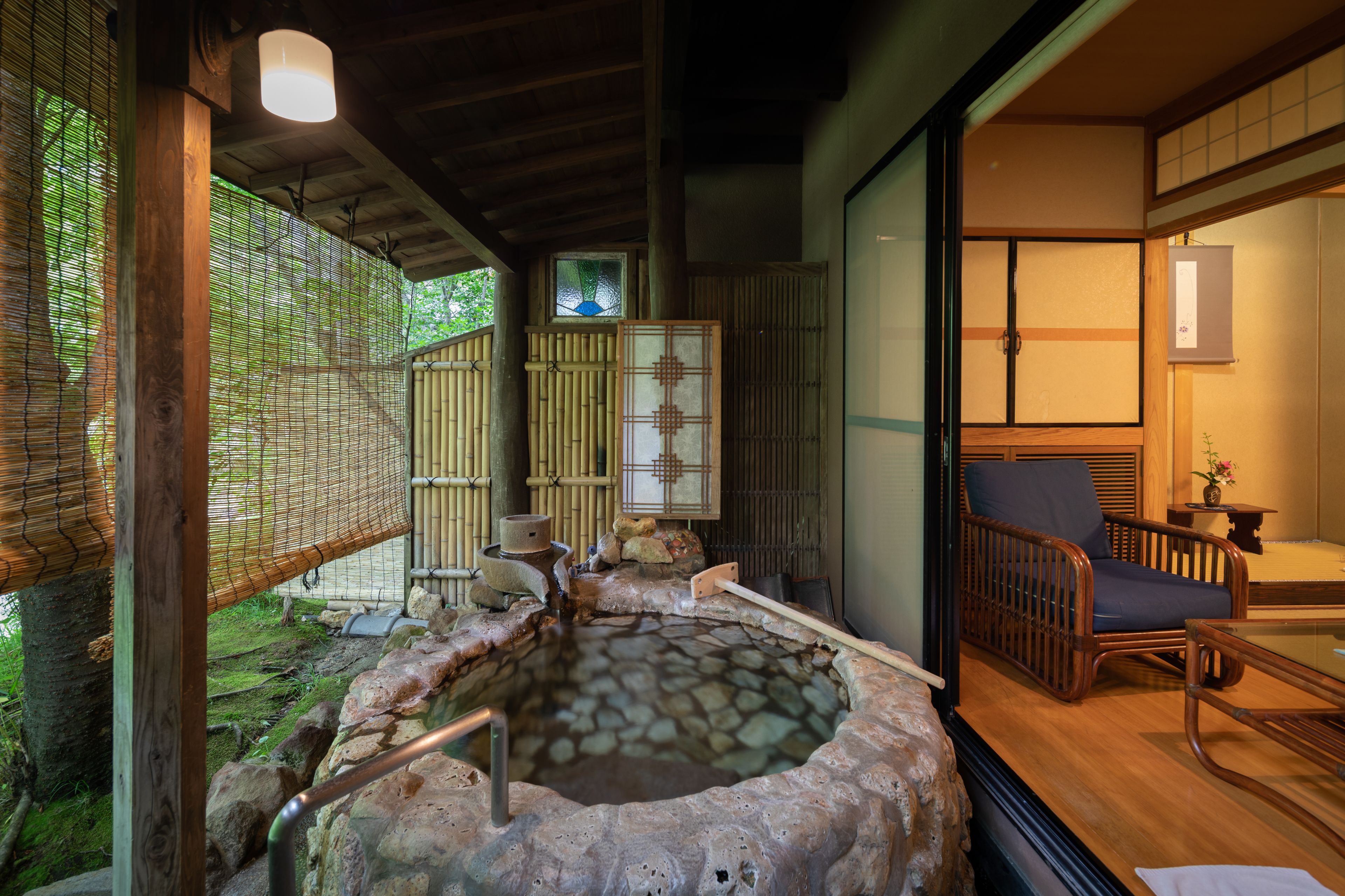 Un onsen japonais traditionnel, avec une source d’eau chaude naturelle entourée de pierres, des meubles en bois et une clôture en bambou.