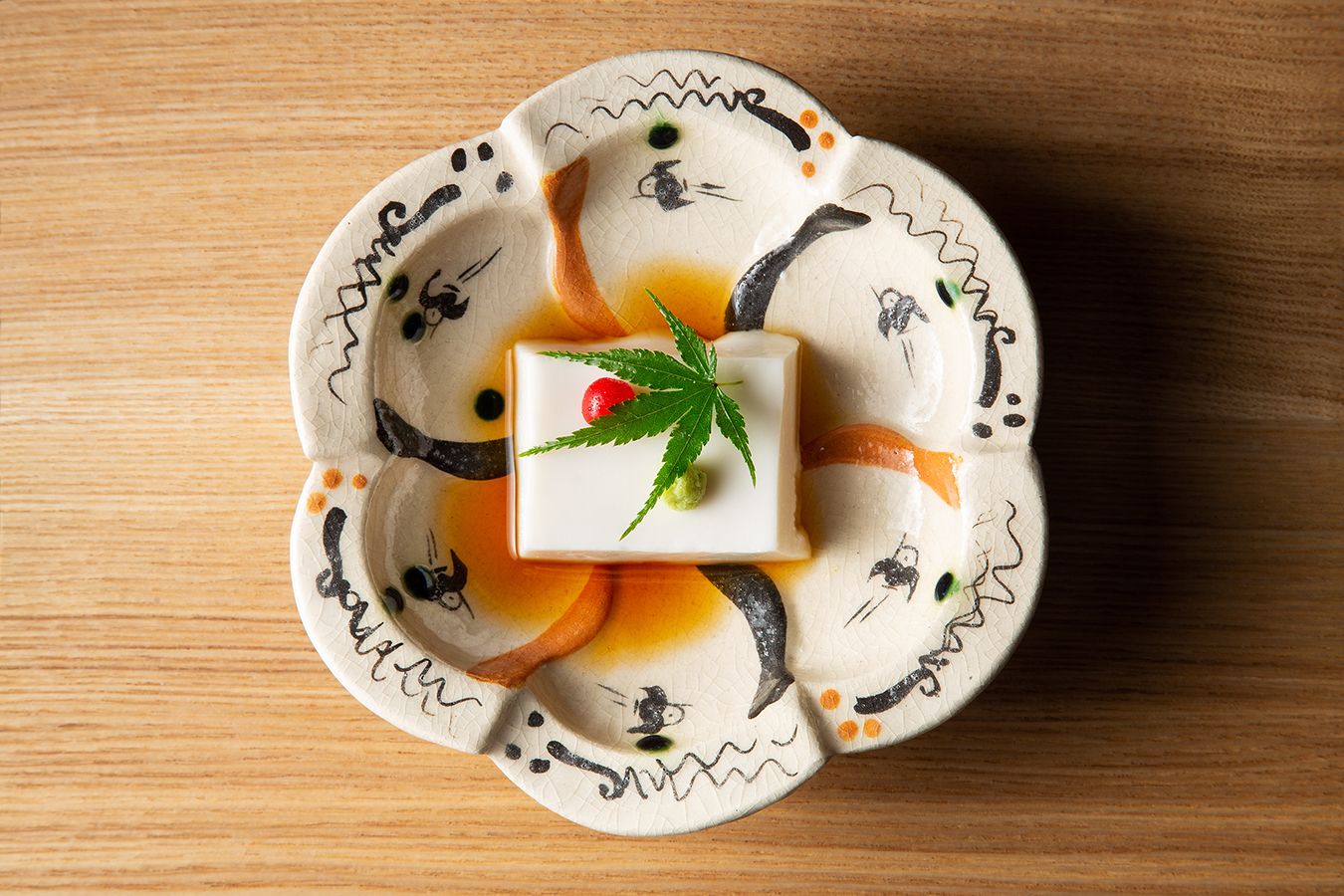 Un dessert de forme carrée, présenté sur une assiette en céramique ornée d’un motif décoratif, et posé sur une surface en bois.