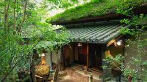 A traditional Japanese building with a thatched roof, surrounded by lush greenery and stone pathways. - Sanso Tensui (Hita)