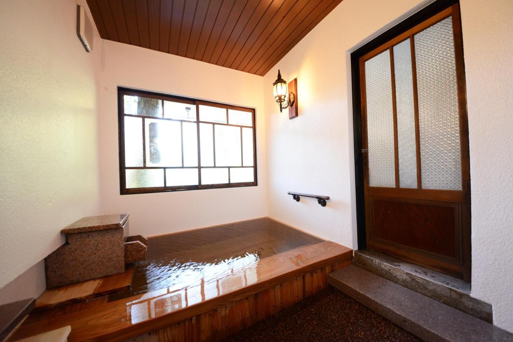 Una habitación japonesa tradicional con suelo de tatami, un banco de madera, una puerta corredera con paneles de vidrio y un aplique de pared.