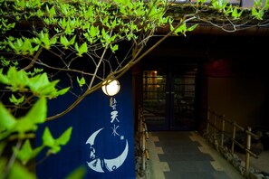 Ein traditioneller japanischer Eingang mit Bambuszaun, Kiesweg und einer hängenden Laterne.