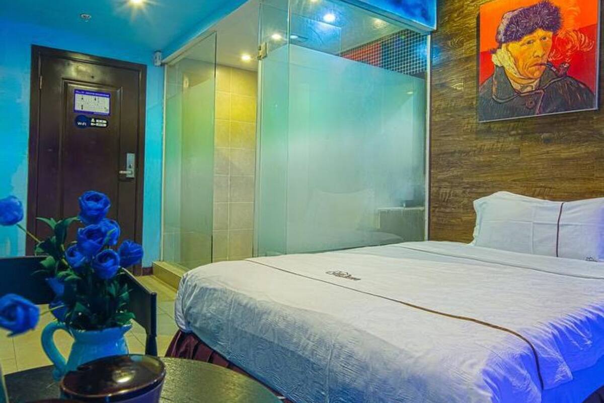 Une chambre d’hôtel avec un lit, une douche en verre, un tableau au mur et un vase avec des fleurs bleues.
