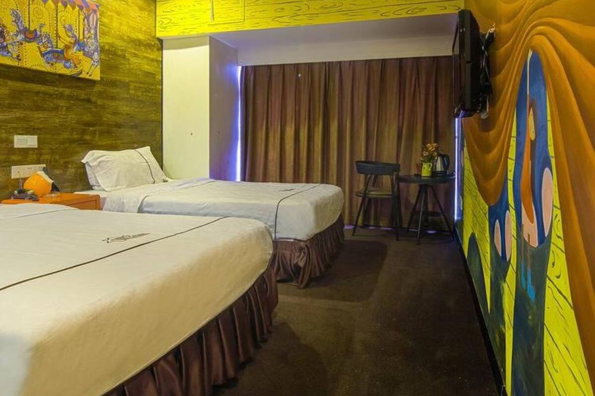 Une chambre d’hôtel avec deux lits, une petite table avec une chaise et un téléviseur fixé au mur.