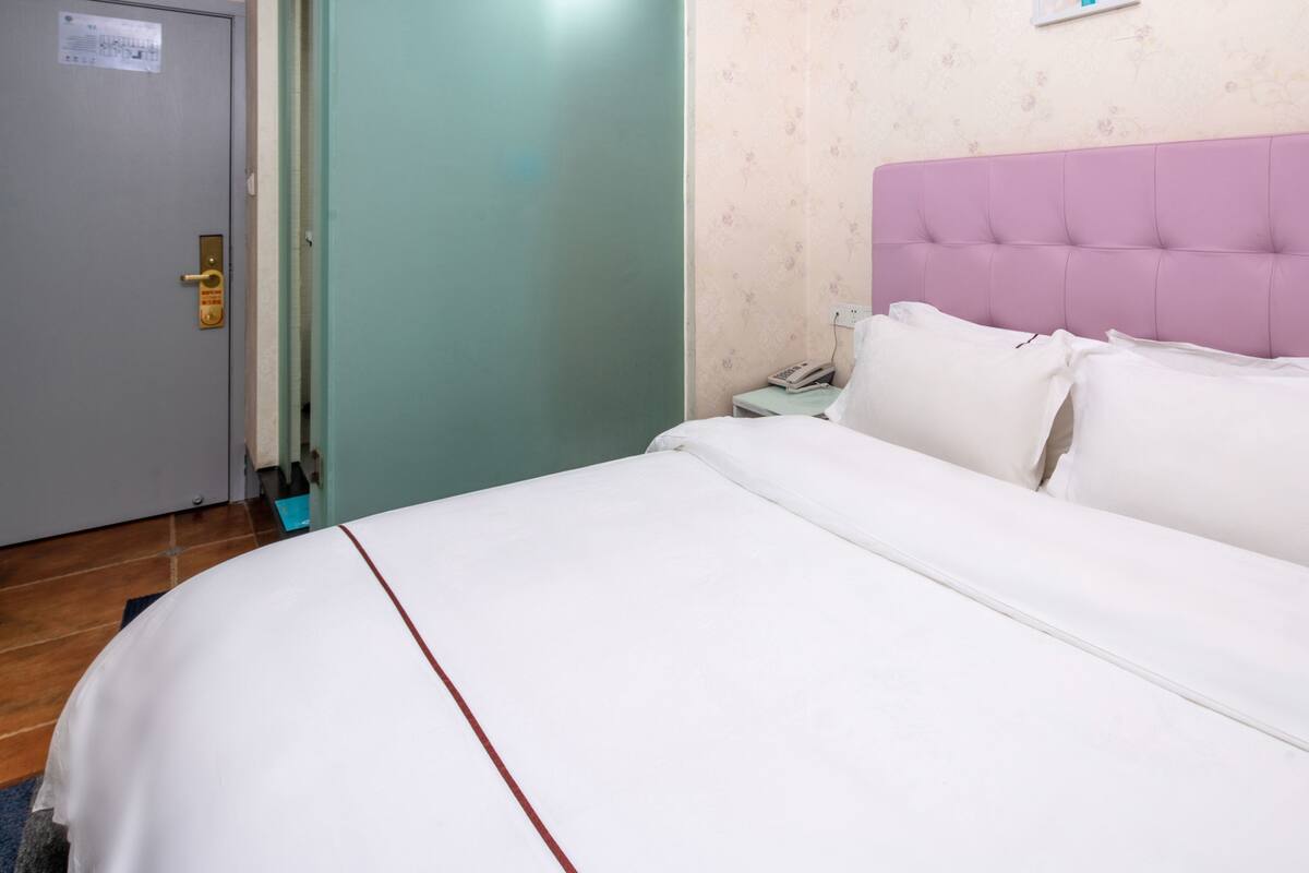 A hotel room with a bed, a nightstand, a telephone, and a door.