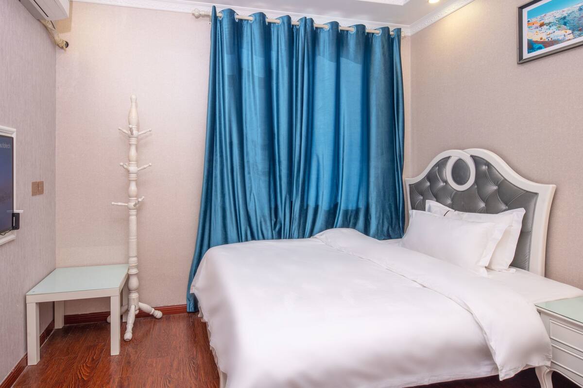 A bedroom with a bed, a bedside table, a TV, and a blue curtain.