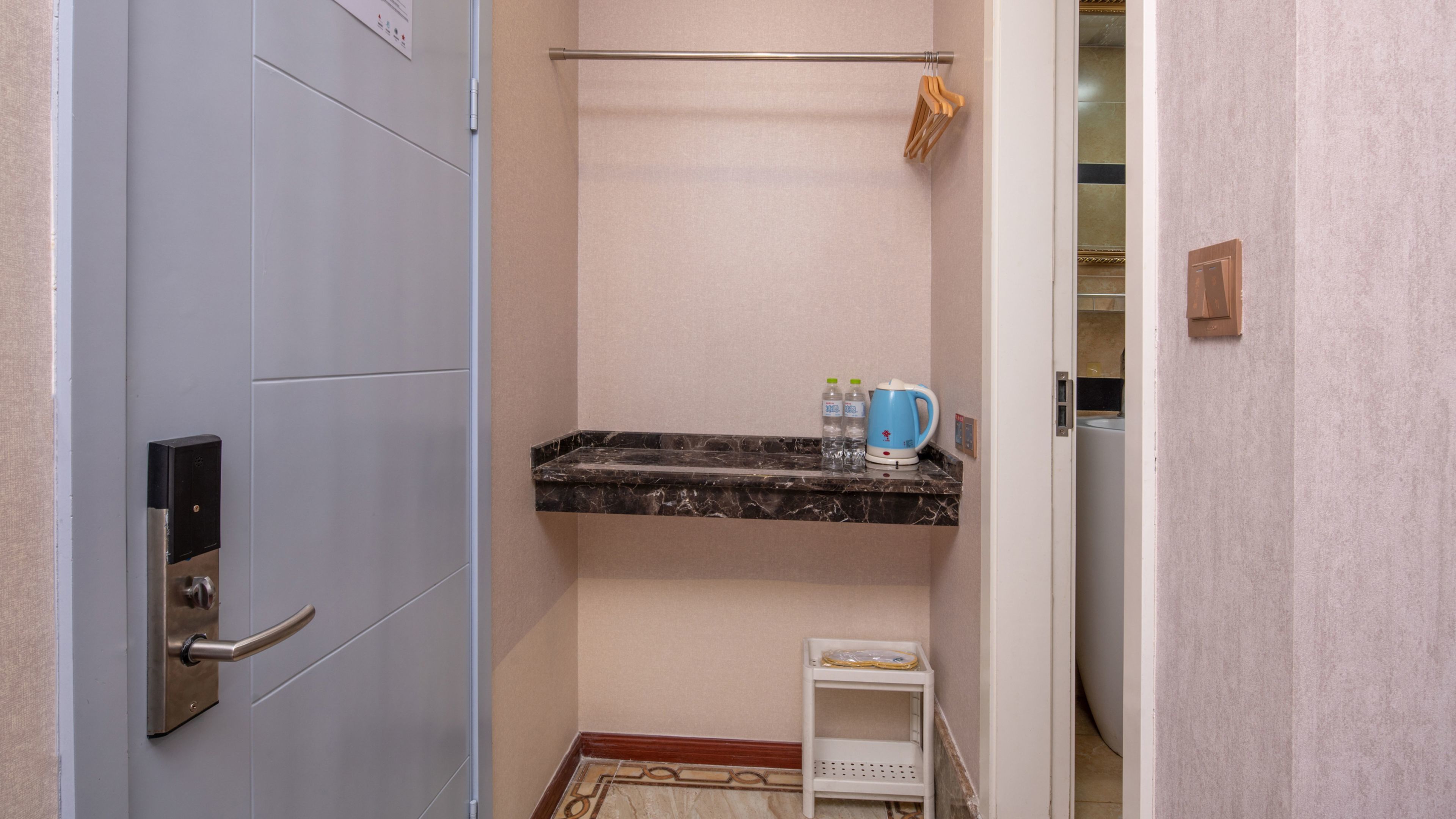 A bathroom with a marble countertop, a towel rack, a small shelf with toiletries, and a door with a handle.