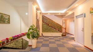 A hotel lobby with a checkered carpet, a staircase with wooden railings, a large potted plant, and a painting on the wall. - Sucha Hotel Chengdu Wuhouci Jinli (Chengdu)