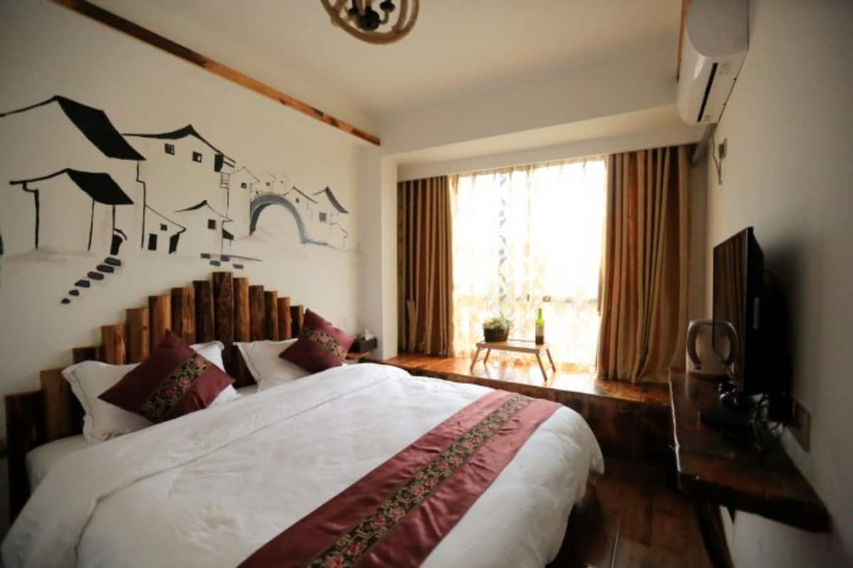Quarto com uma cama grande, cabeceira de madeira, painel decorativo na parede, janela com cortinas e uma escrivaninha com cadeira.