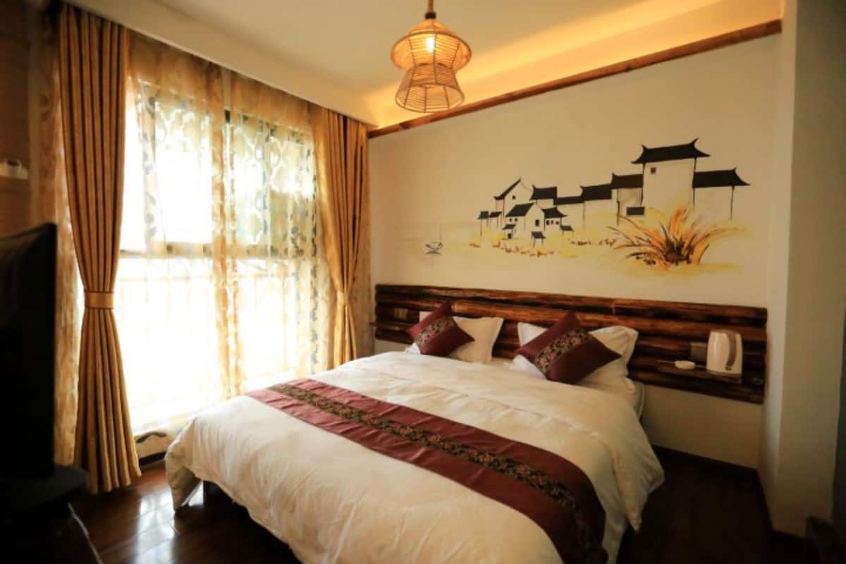 Quarto com cama grande, cabeceira de madeira e pintura na parede retratando edifícios tradicionais.