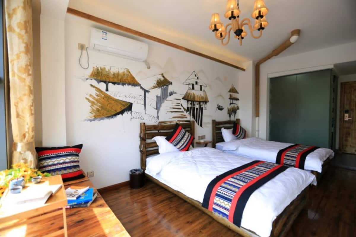 Quarto com duas camas, cabeceiras de madeira, uma mesa de madeira com uma planta e um mural na parede.