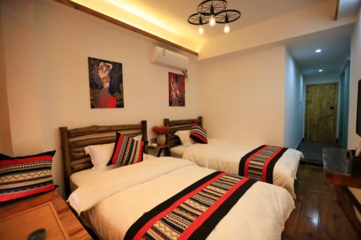 Quarto de hotel com duas camas, cabeceiras de madeira, colchas estampadas e duas unidades de ar condicionado fixadas na parede.
