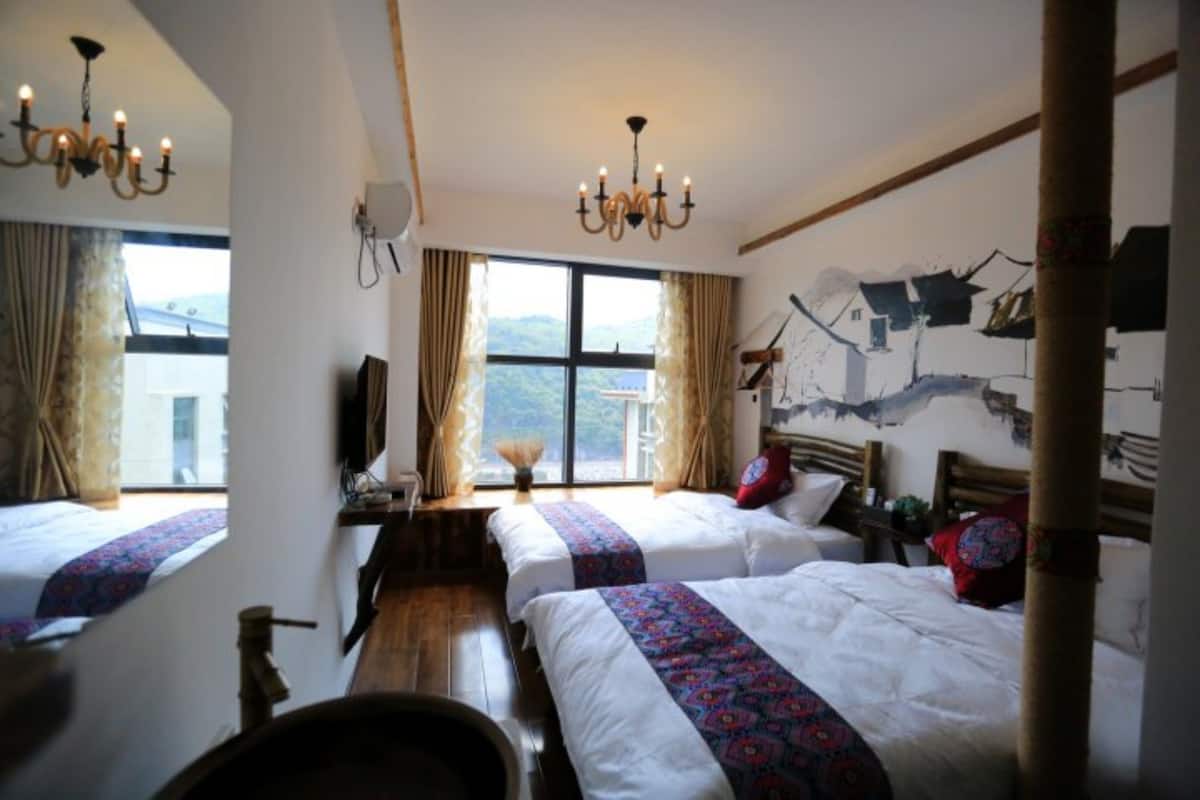 Quarto de hotel com duas camas, uma escrivaninha de madeira, um candelabro e uma janela grande com vista para as montanhas.
