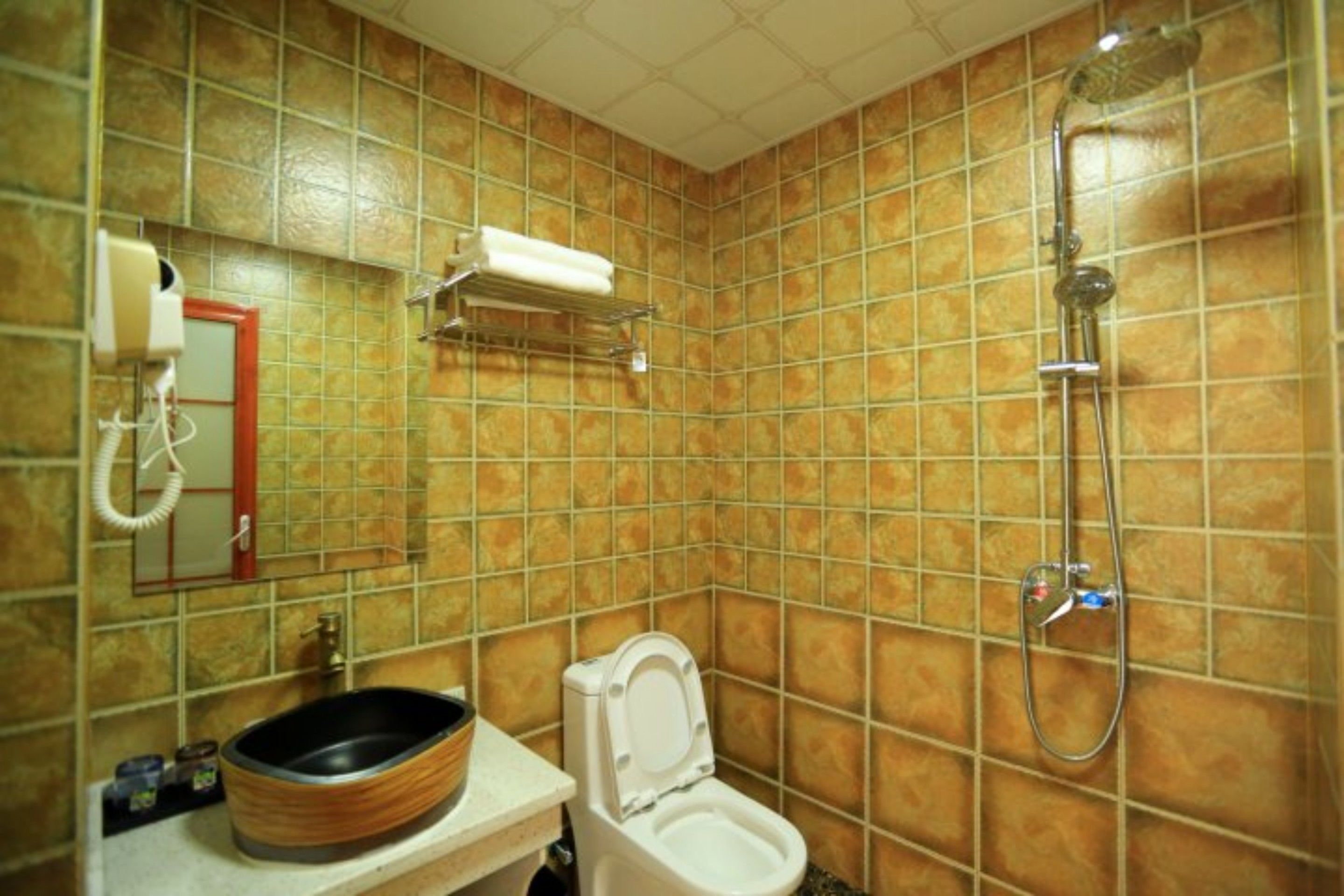Une salle de bain avec des toilettes blanches, un lavabo avec un récipient en bois, une douche et un porte-serviettes.