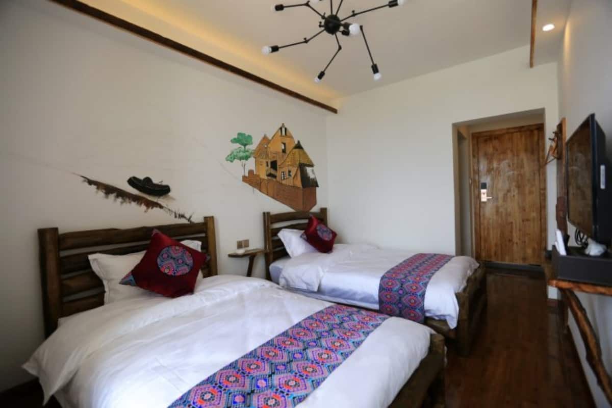 Quarto com duas camas, cabeceiras de madeira, ventilador de teto, porta de madeira e televisão fixada na parede.