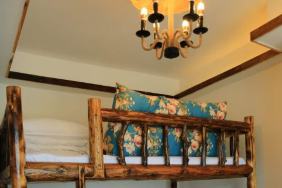 Uma cama beliche com estrutura de madeira e almofadas estampadas com motivos florais.