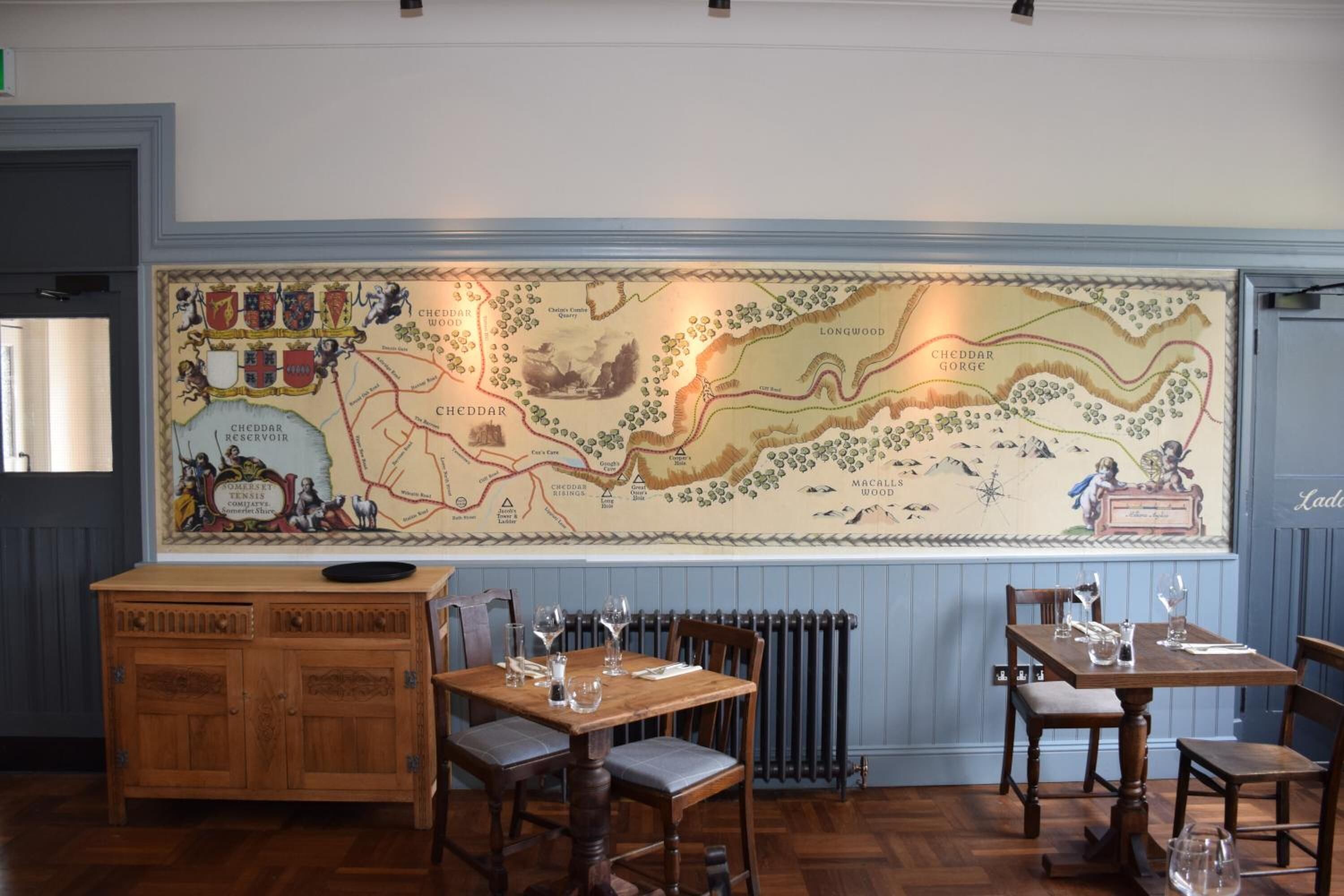 A restaurant interior with a large map on the wall, wooden furniture, and a radiator.