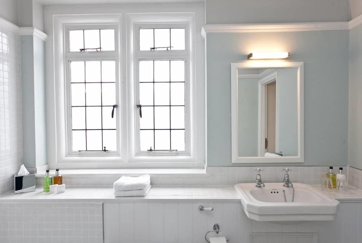 A bathroom with two windows, a sink, and a mirror.