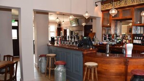 Zona de bar con taburetes de madera, barra y exhibición de vinos.