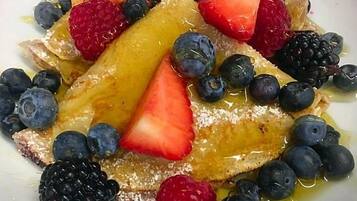 A plate of pancakes topped with strawberries, blueberries, raspberries, and blackberries, drizzled with syrup.