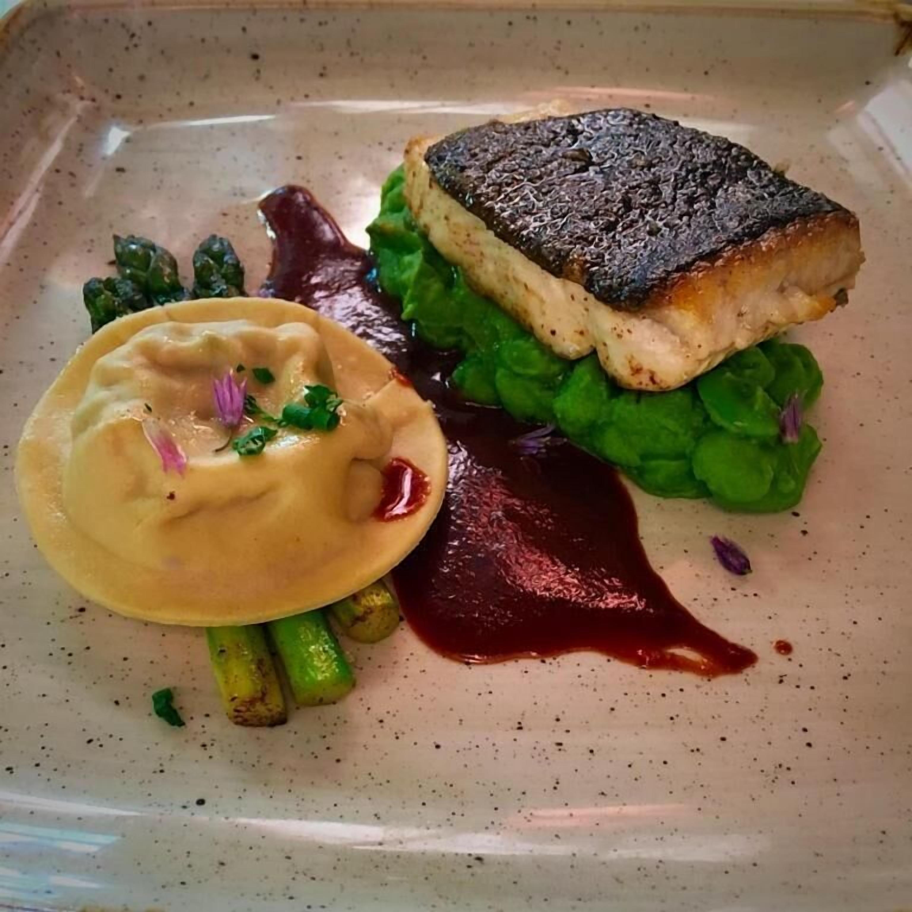 Une assiette contenant un morceau de poisson grillé, des asperges et une sauce crémeuse.