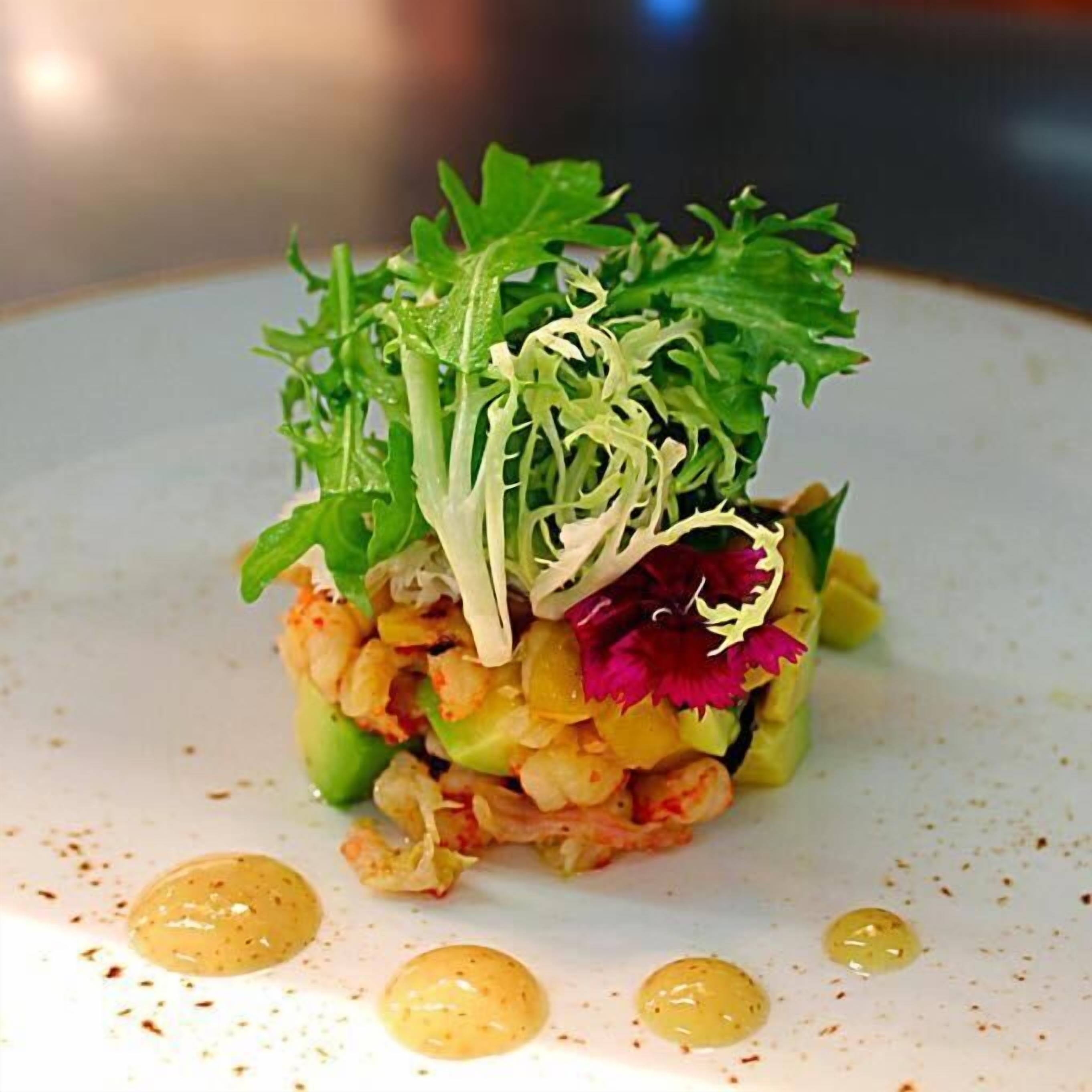 A dish with greens, shrimp, and a flower on a plate.