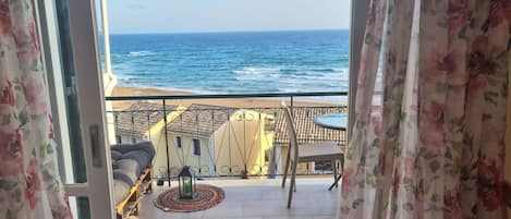 A balcony with a view of the sea, a table with chairs, and a small rug.