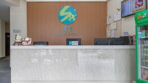 A reception desk with a wooden panel wall, a sign for Sujoha Hotel, a digital screen displaying room information, and a vending machine with beverages. - Sucha Hotel Wuhan Hankou Railway Station (Wuhan)