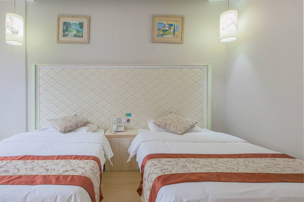 Ein Hotelzimmer mit zwei Betten, einer gesteppten Kopfteil, Nachttischen mit Lampen und zwei gerahmten Bildern an der Wand.