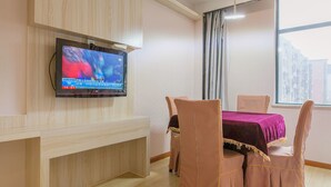 A hotel room with a flat-screen TV mounted on the wall, a wooden desk, a table with a purple tablecloth, and four chairs with yellow trim. - Sucha Hotel Wuhan Hankou Railway Station (Wuhan)