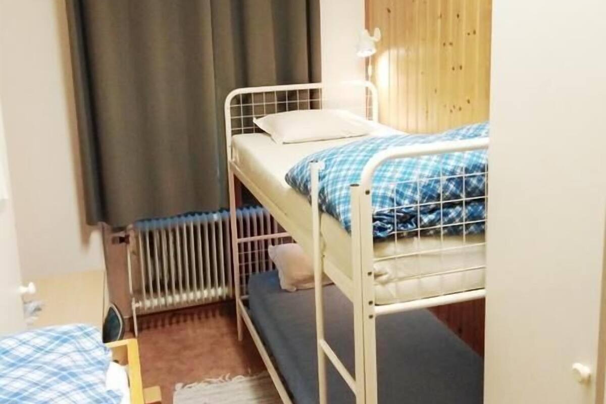 Een slaapkamer met stapelbed, een houten paneelwand, een radiator en een raam met gordijnen.