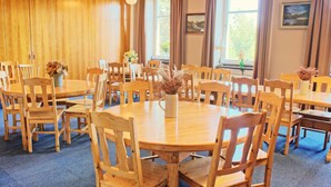 Una habitación con varias mesas y sillas de madera dispuestas en círculo, con un jarrón de flores secas en cada mesa.