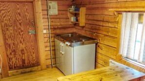 Interior de una cabaña de madera con kitchenette, una mesa de comedor y una ventana.