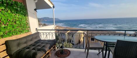 A balcony with a black sofa, a round table, and chairs, overlooking the ocean.