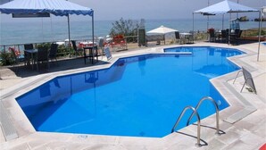 A swimming pool with a clear view of the ocean, surrounded by lounge chairs and umbrellas. - Corfu Island Apartment 149 (Corfu)