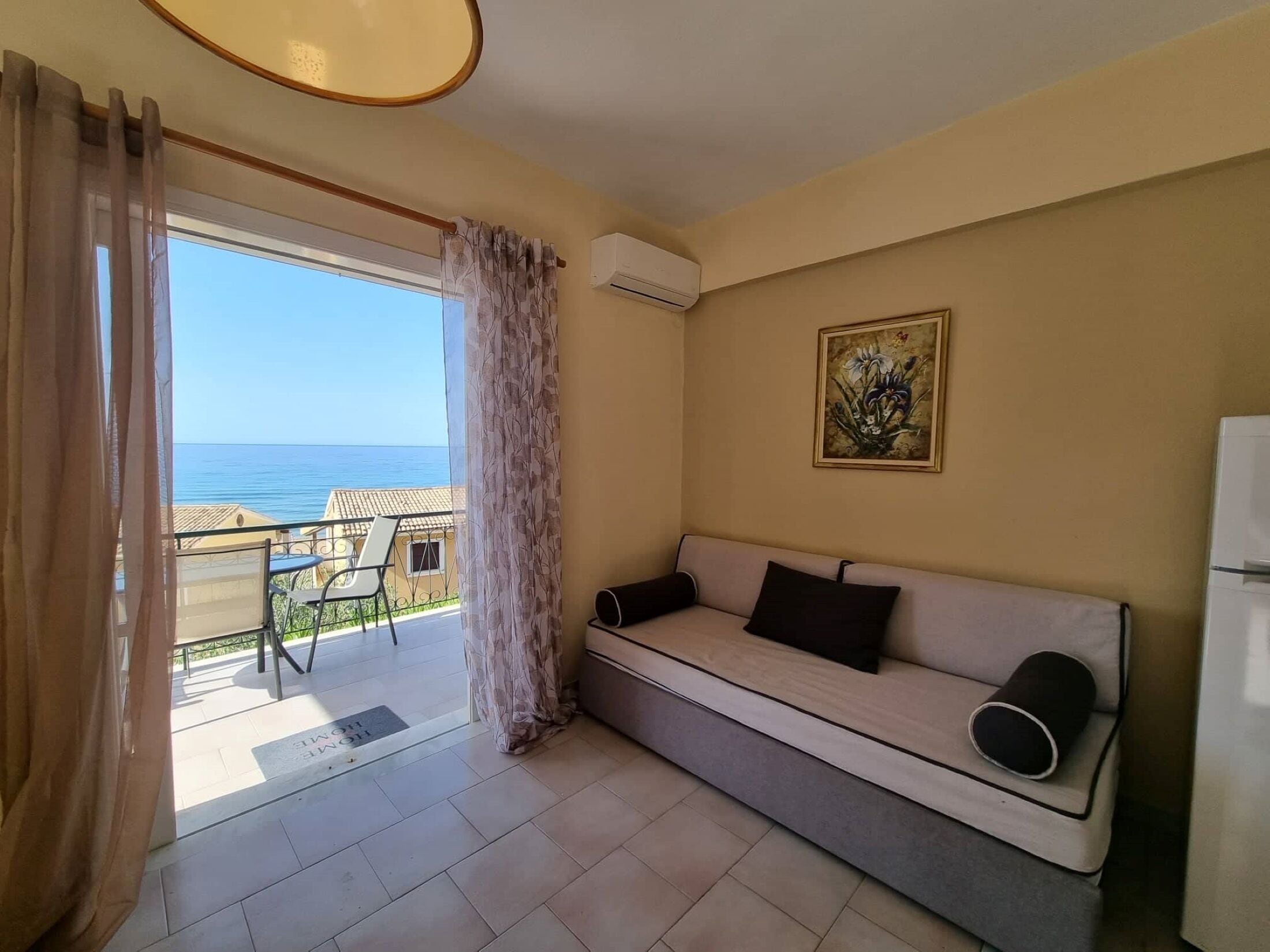 A room with a sofa, a painting, and a view of the sea.