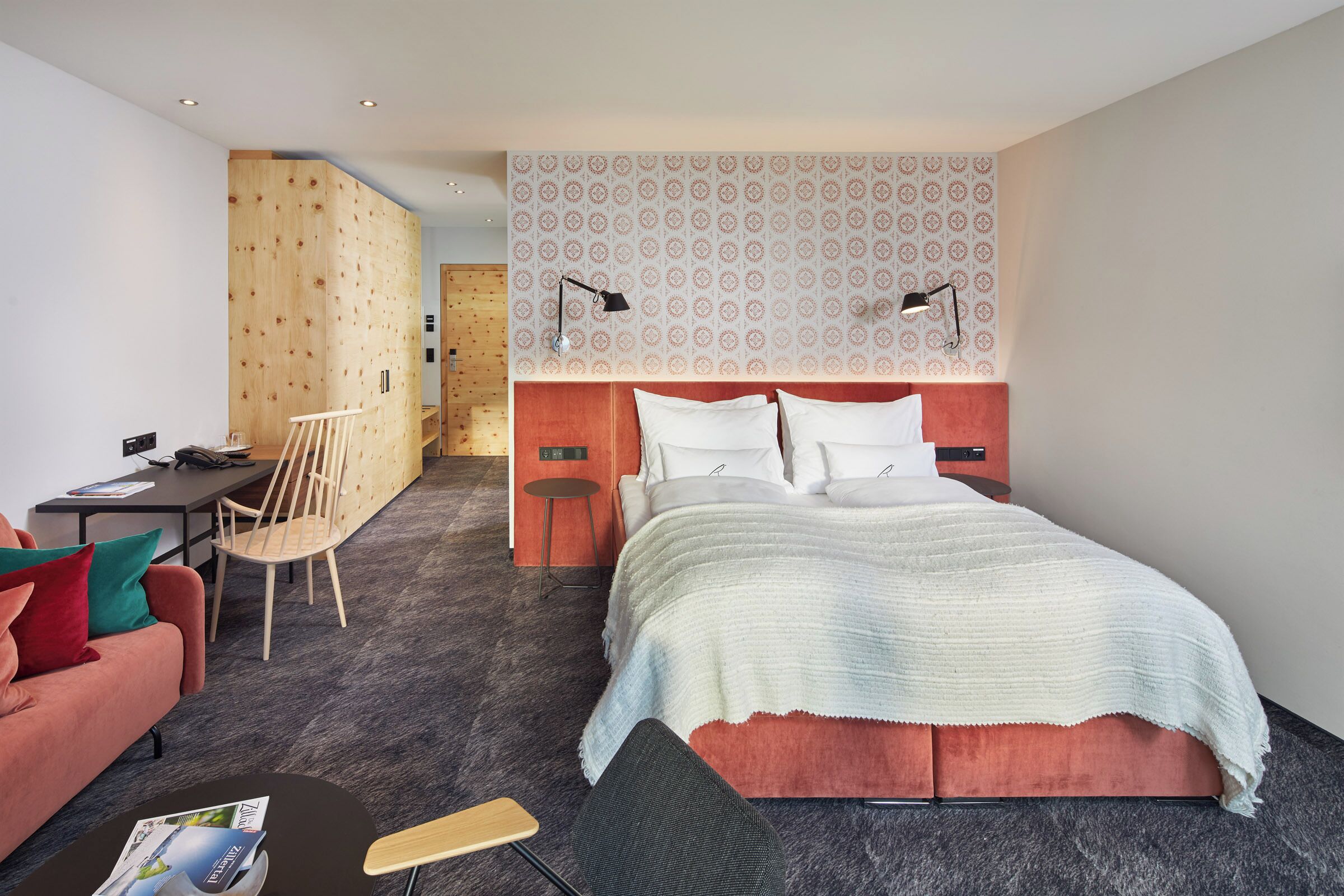 Ein modernes Hotelzimmer mit einem großen Bett, einem Schreibtisch, einem Sessel und einem kleinen Tisch.