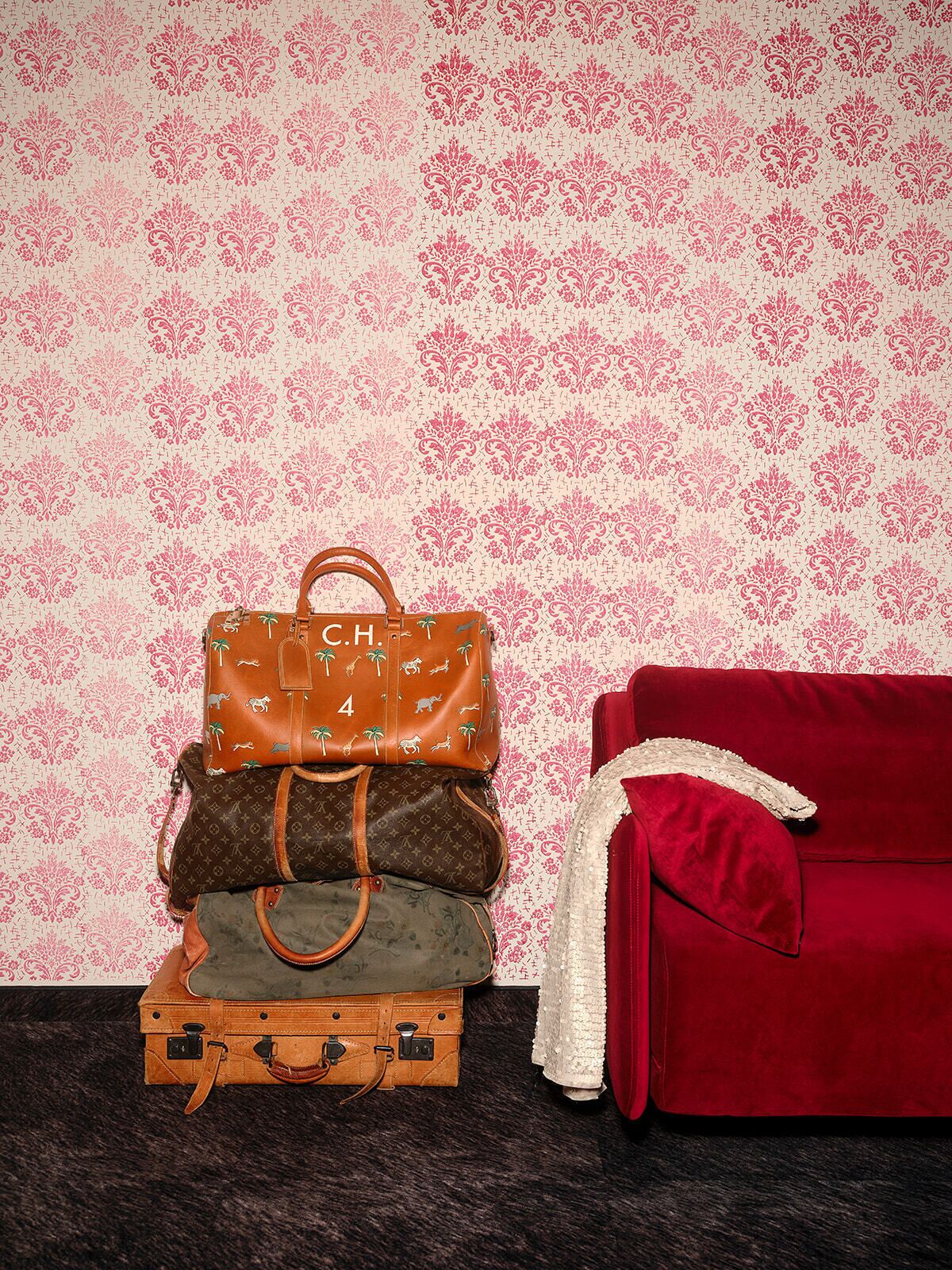 A stack of three handbags against a patterned wallpaper, with a red sofa and a white blanket in the foreground.
