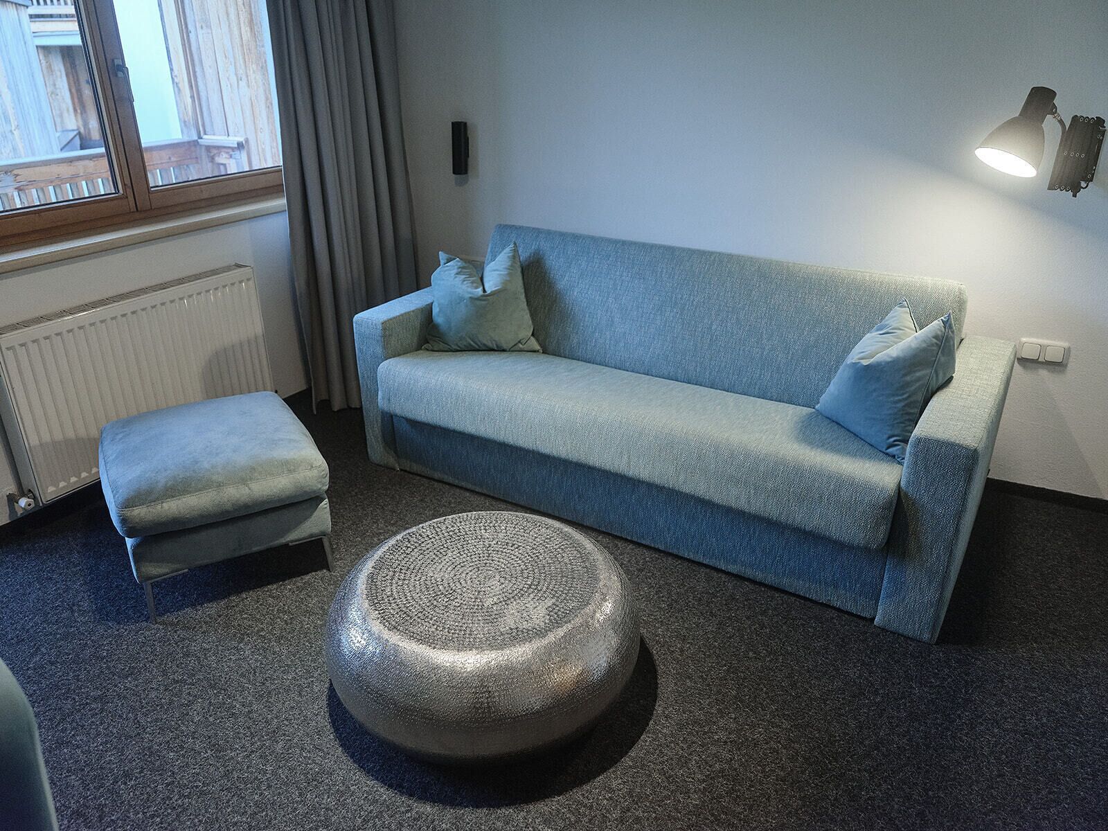 A modern living room with a grey sofa, a matching ottoman, and a round, textured coffee table.