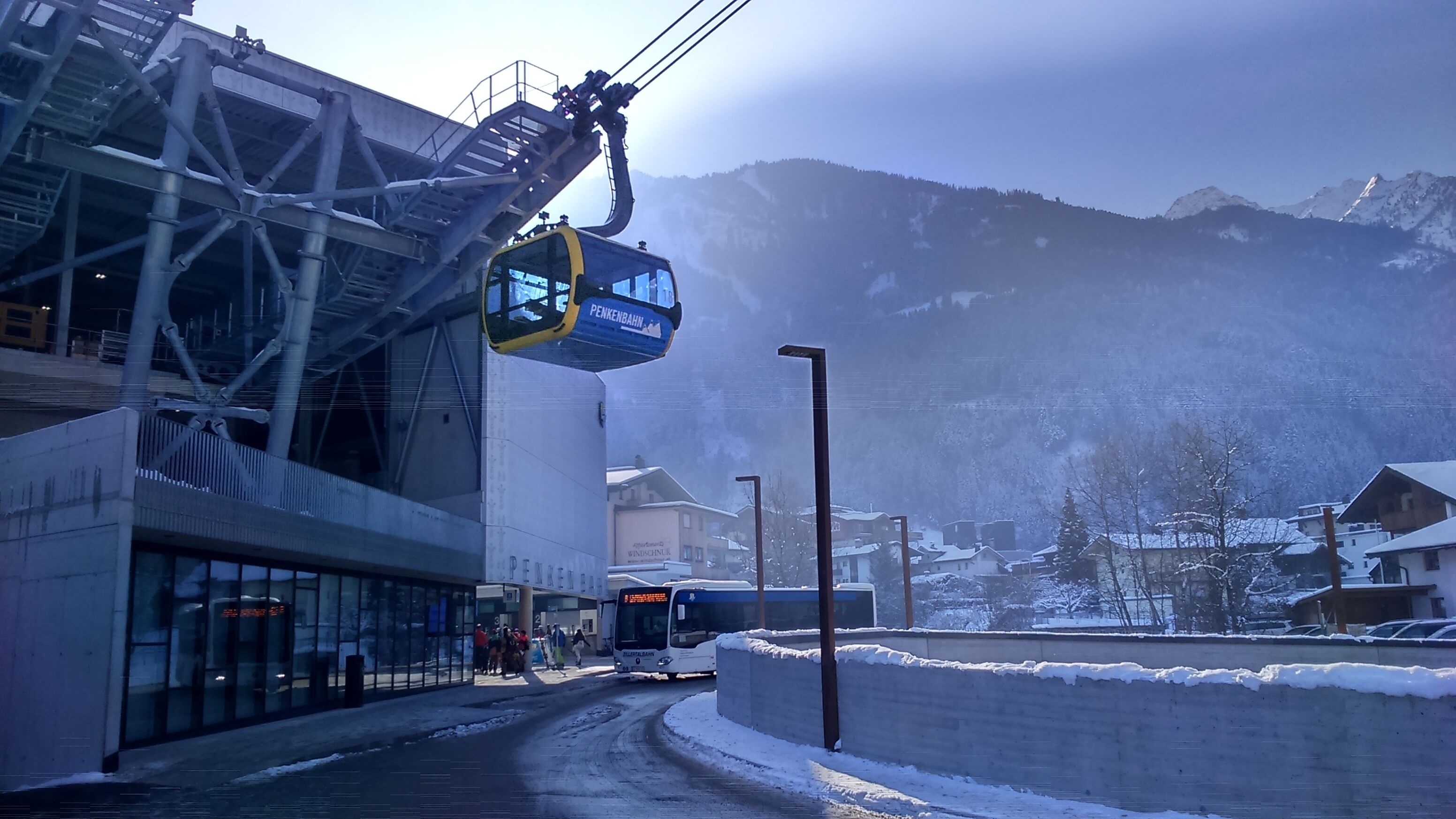 A ski lift chair suspended from a metal structure, a bus, and a snowy mountain backdrop.