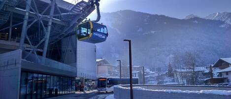 A ski lift chair suspended from a metal structure, a bus, and a snowy mountain backdrop.