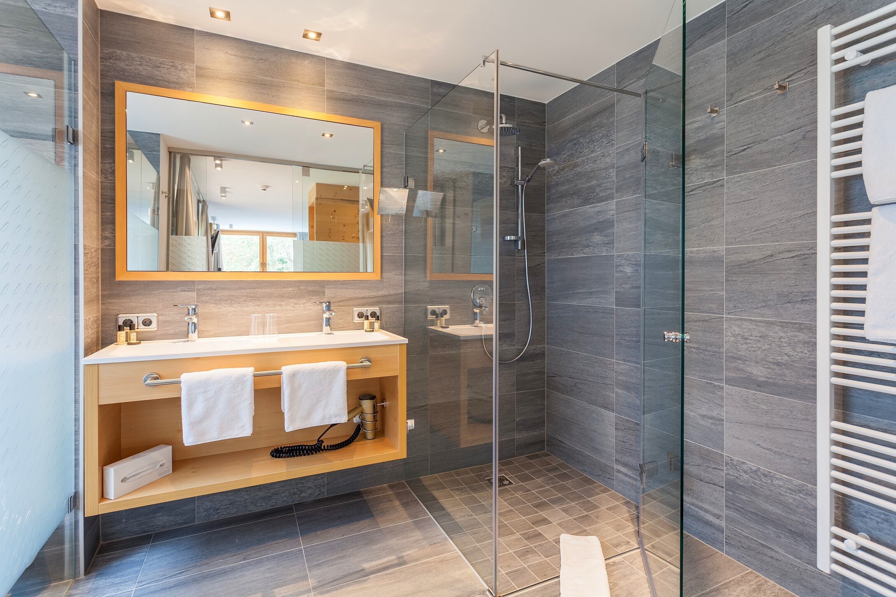A modern bathroom with a glass shower enclosure, a large mirror, and a wooden vanity with a towel rack.